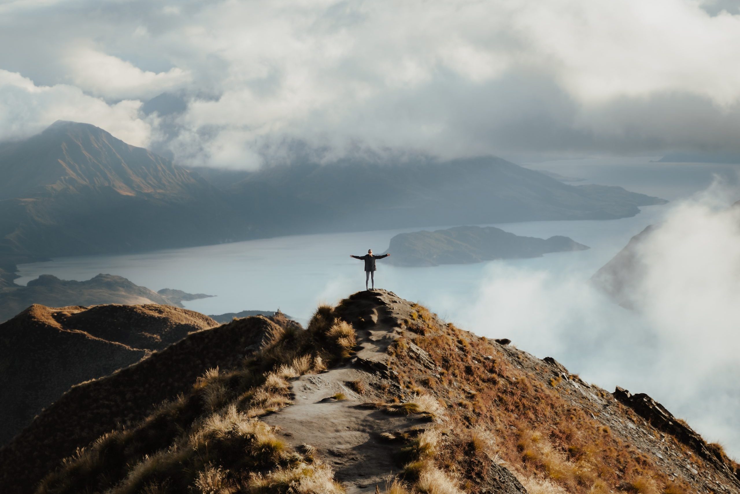 A man with hands wide open standing at the top of a mountain enjoying the incredible view of a lake